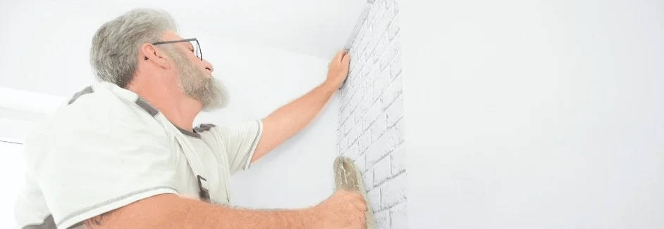 Person bringt Tapete mit Ziegelsteinmuster an